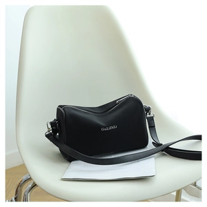 Détail du sac bandoulière cylindrique noir avec logo posé sur une chaise blanche