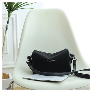 Détail du sac bandoulière noir posé sur une chaise avec logo et bandoulière grainée