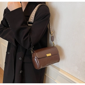 Close-up of brown leather crossbody bag with vintage geometric strap and gold buckle