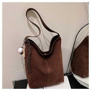 Detail der dunkelbraunen Wildleder-Hobo-Tasche mit grober Naht und Baseball-Anhänger