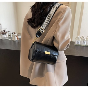 Detail of a black patent leather shoulder bag with a geometric woven strap in a cafe