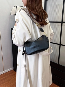 Black leather hobo bag with wide geometric woven strap and gold hardware on white coat