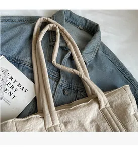 Detail of beige quilted tote bag with soft padded handles on blue denim background