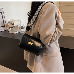 Detail of black glossy crossbody bag with geometric weave strap and gold buckle