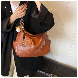 Détail d'un sac à bandoulière vintage marron avec pendentif baseball et bouton-pression métal