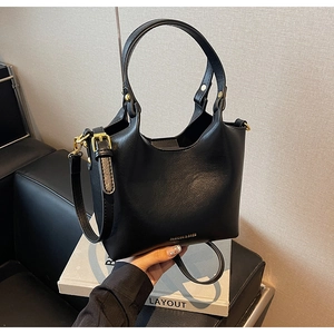 Vue de dessus d'un sac seau en cuir noir avec détails dorés sur un livre blanc