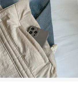 Close-up of a quilted shoulder bag showing a side zipper pocket holding a large smartphone