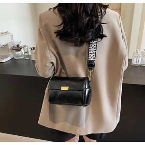 Detail of black glossy leather crossbody bag with geometric woven strap and gold buckle