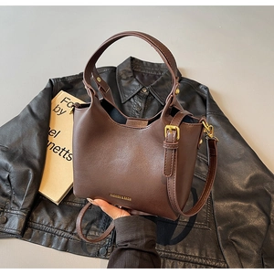 Détail d'un sac seau en cuir marron foncé avec finitions dorées sur une veste noire