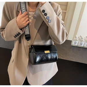 Detail of glossy black leather crossbody bag with geometric woven strap and gold buckle