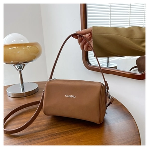Détail du sac cylindrique en cuir marron avec logo et bandoulière amovible