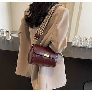 Detail of burgundy oil-wax leather bag with wide geometric strap and metal hardware