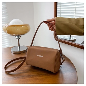 Détail d'un sac polochon en cuir marron avec logo sur une table en bois rustique