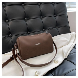 Gros plan d'un sac Boston marron foncé en cuir mat sur un canapé de luxe