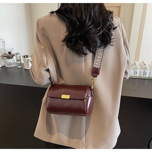 Detail of burgundy crossbody pillow bag featuring wide herringbone strap and gold buckle