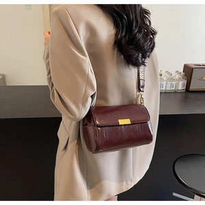 Detail of burgundy patent leather crossbody bag with ethnic patterned woven wide strap