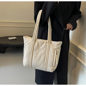 Detail of off-white tote bag with woven zipper puller shown against a black coat