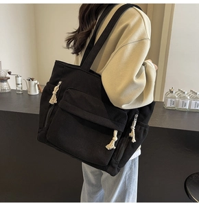 Détail du sac cabas en velours côtelé noir montrant la poche à rabat et le gland en coton