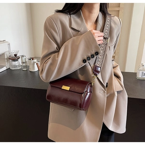 Detail of burgundy glossy leather crossbody bag with wide patterned strap and metal buckle