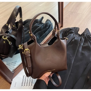 Détail du sac à main en cuir marron foncé avec clous dorés et logo de marque embossé