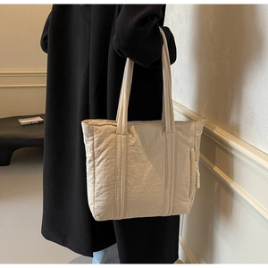 Detail view of beige textured tote bag with wide straps and side zipper on a shoulder