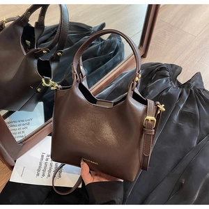 Détail d'un sac seau en cuir marron foncé avec boucles dorées sur tissu noir