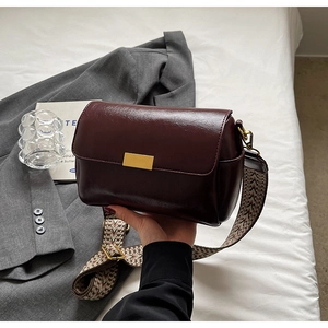 Detail of burgundy leather crossbody bag with wide patterned jacquard strap and gold clasp