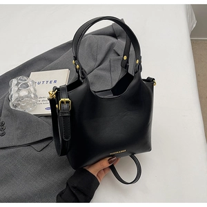 Détail du sac seau noir mat avec rivets dorés et logo sur fond de costume gris