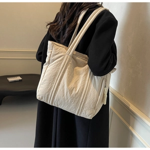 Detail of a beige quilted tote bag with textured finish shown on a shoulder