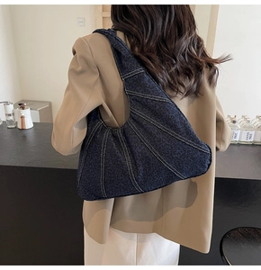 Detail of dark blue denim crescent bag with white contrast stitching on a brown blazer