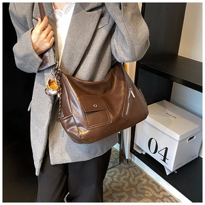 Détail du sac à bandoulière en cuir marron rétro porté sur un blazer en laine gris