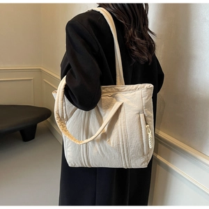 Detail of a beige quilted nylon tote bag showing the side zipper and knotted puller