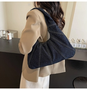 Detail of dark blue denim underarm bag featuring white contrast stitching and texture