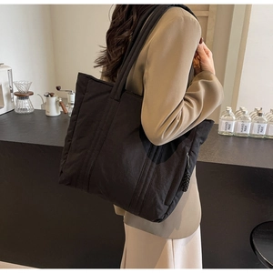 Close-up of a black nylon tote bag with side zipper detail in a modern cafe setting