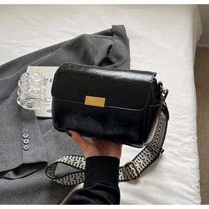 Detail of glossy black shoulder bag featuring gold buckle and geometric woven strap