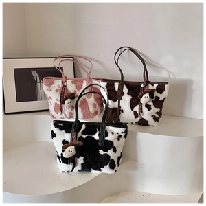 Detailed view of three plush cow print tote bags in pink, brown and black with cute charms