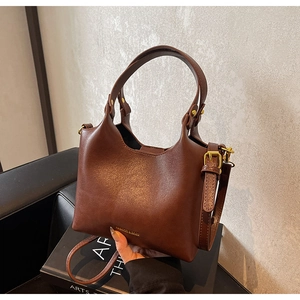 Gros plan du sac à main en cuir marron foncé avec logo doré et bandoulière réglable