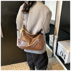 Détail du sac bandoulière en cuir marron avec poche à rabat avant et breloque fromage