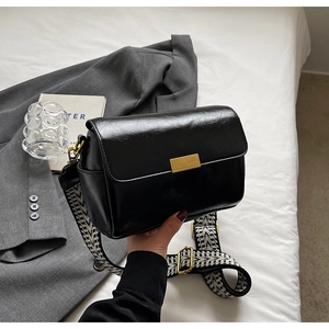 Detail of black glossy handbag with gold rectangular lock and patterned wide shoulder strap