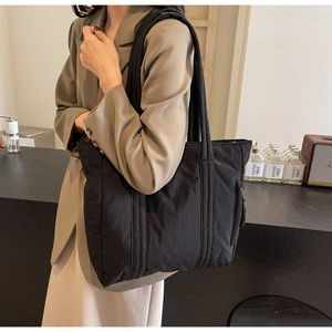 Fashionable black quilted nylon tote bag worn on shoulder by model in a cafe setting