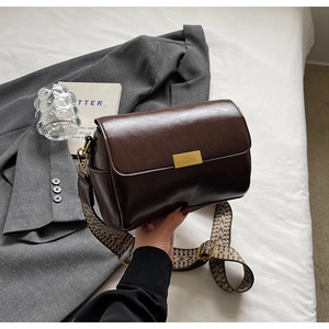 Detail of vintage coffee brown crossbody bag featuring wide embroidered strap and gold buckle