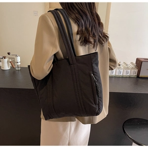 Detail of the side zipper pocket and soft quilted fabric texture on this black tote bag