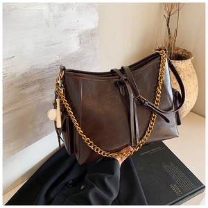 Dettaglio borsa tote marrone scuro con catena dorata, pelle liscia e ciondolo da baseball