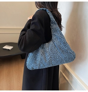 Detailed side view of large blue leopard print hobo bag worn by a model in black coat