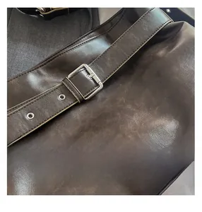 Detail of adjustable silver buckle and eyelets on a dark brown leather tote bag