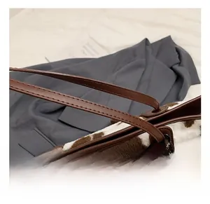 Detailed view of the brown leather handles and cow print plush tote bag with accessory