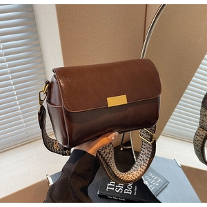 Detail of vintage brown glossy leather pillow bag with wide geometric woven shoulder strap