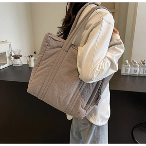 Detail of grey quilted tote bag featuring woven zipper pulls and wide shoulder straps