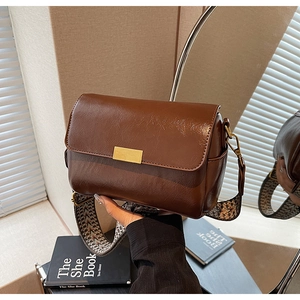 Detail of a brown leather crossbody bag with a geometric pattern wide woven strap