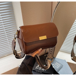 Close-up of vintage dark brown faux leather pillow bag with wide jacquard strap and gold buckle
